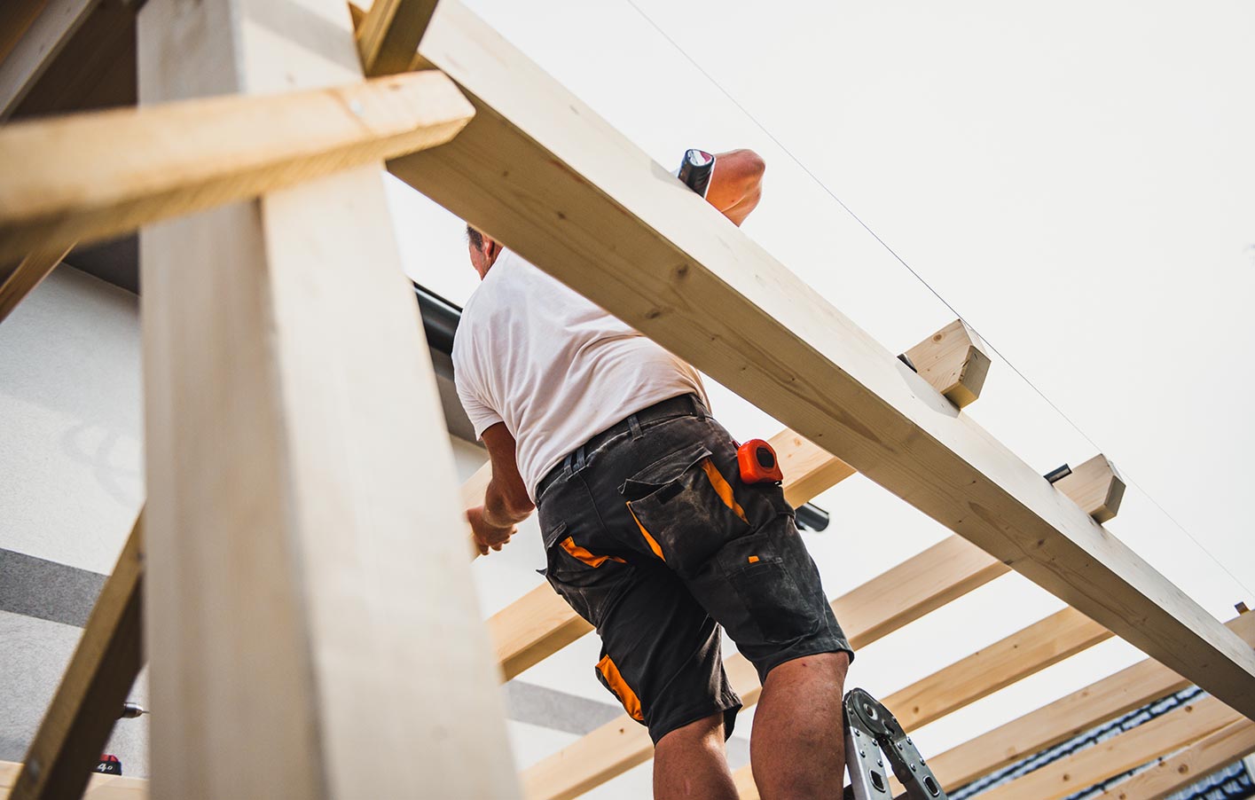 Handwerker auf Leiter befestigt Holzbalken für die Terrassenüberdachung.